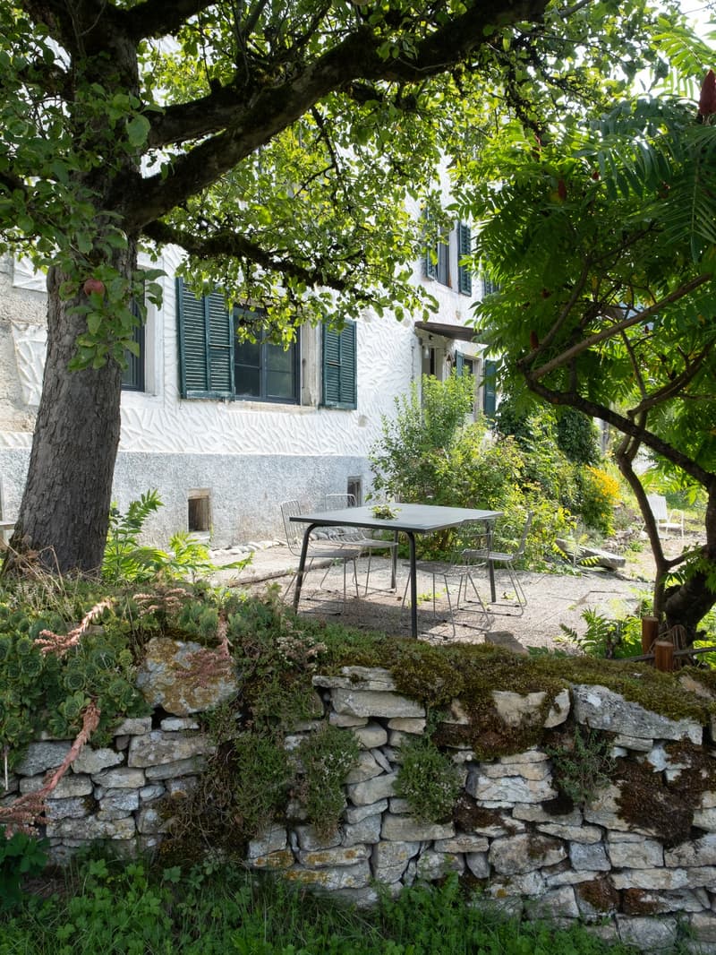 White painted house, stone walls, large windows, garden, stone table with chairs, moss and lichen on stones