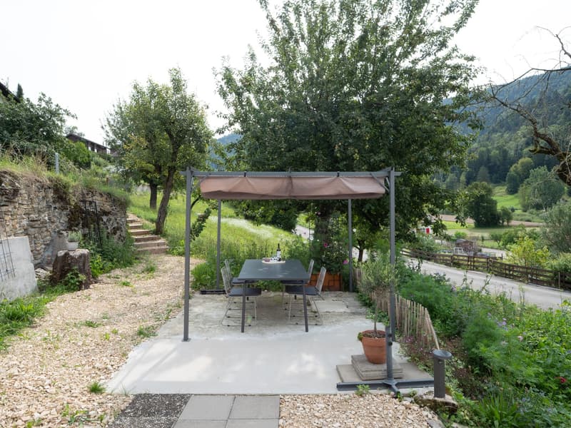 covered dining area with table and chairs, gravel floor, trees, potted plants, mountain view
