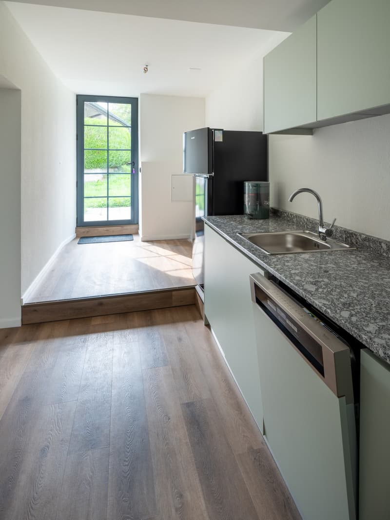 Contemporary kitchen with granite countertops, stainless steel sink, modern faucet, refrigerator, and dishwasher under the counter, wooden floor, and a glass door leading to an outdoor area.