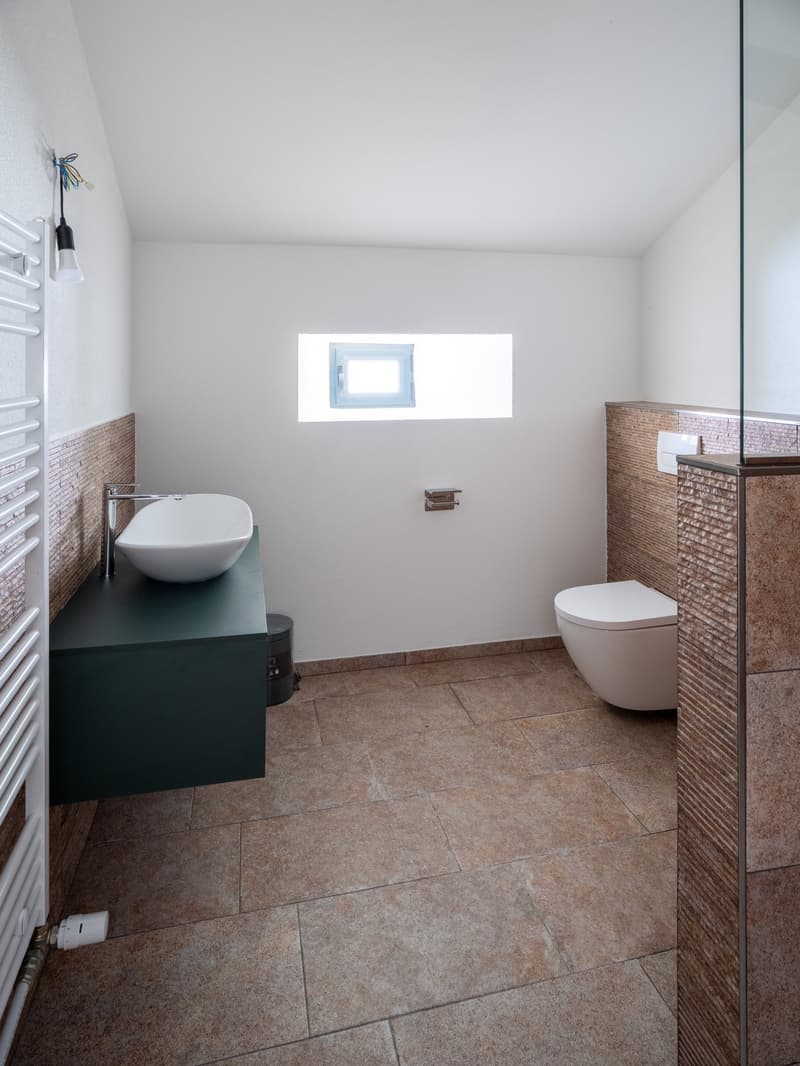 small modern bathroom with sink, toilet, window, heater, and tiled flooring