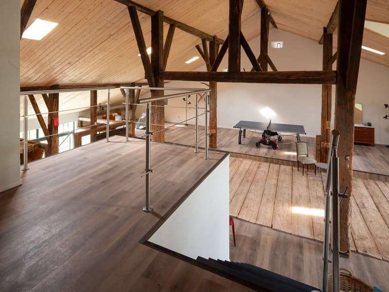 a wooden interior with a metal railing in the middle, a wooden floor, a table tennis game, chairs, and a cabinet with a mirror