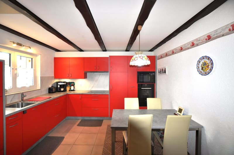 Red kitchen cabinets, tiled backsplash, black oven, microwave, coffee machine, dining table, chairs, pendant light, framed artwork, power outlet