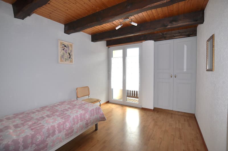 small bedroom, pink bedspread, chair by glass doors, wooden floor, white walls, wooden ceiling