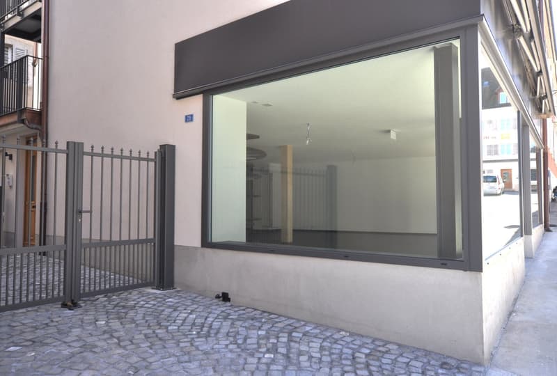 Facade of a building with a large glass window, metal gate, cobblestone pavement, and a balcony on the upper floor.