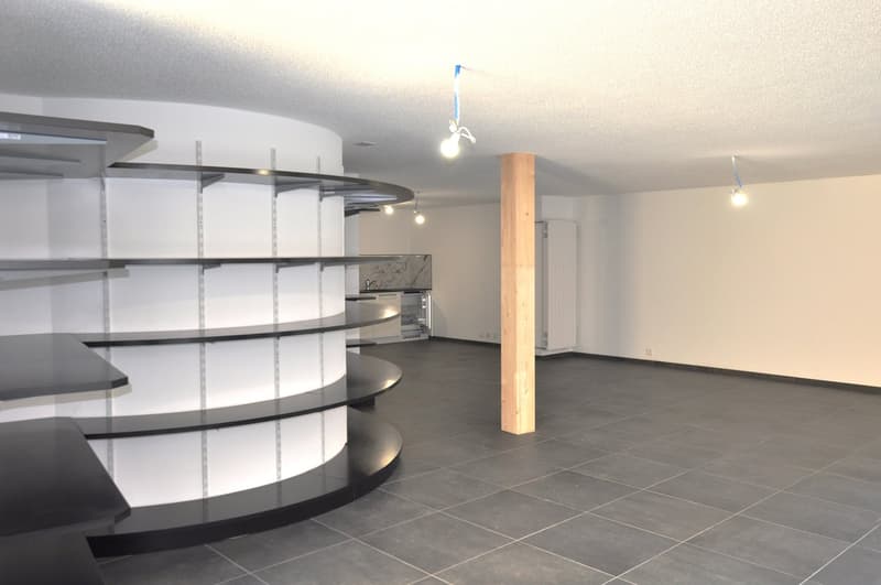 A circular room with a large open shelving system. The shelves are gray and white, with an angular design. The room features dark gray tiled flooring and modern lighting fixtures mounted to the ceiling.