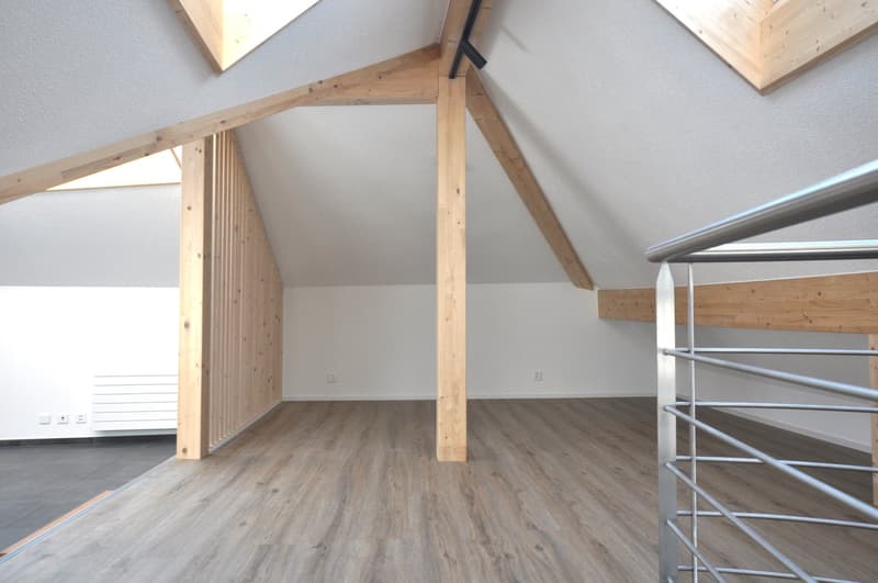 Empty attic room with wooden columns, wooden ceiling beams, and hardwood floors.