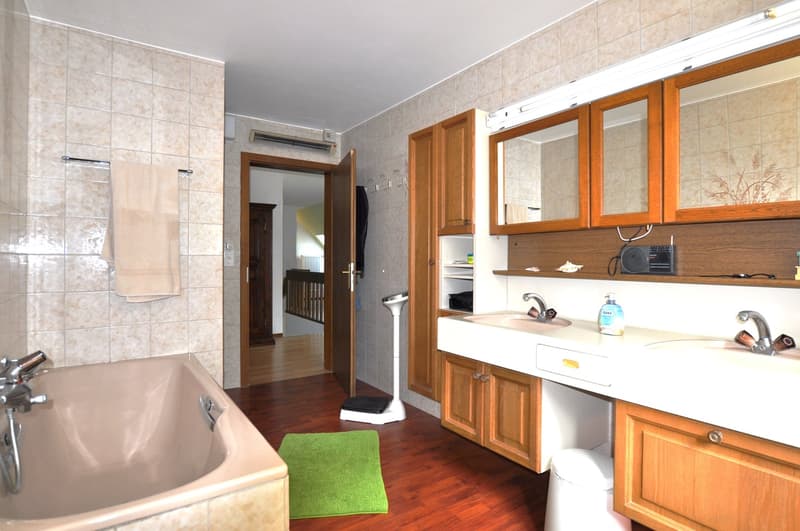 bathroom with bathtub, sink, mirrors, wooden cabinets, towels, green rug, wooden floor, and scale