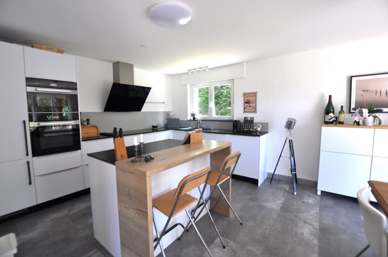 modern kitchen with white cabinets, wooden island, black countertops, built-in oven, stove, sink, faucet, chairs, tripod, bottle, picture frame
