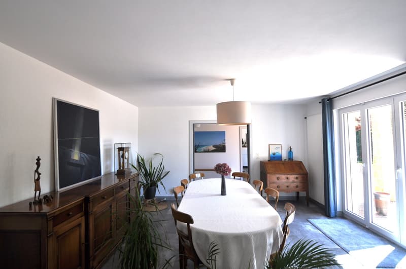 dining room with long table, 8 chairs, large painting, wooden cupboard, desk, sliding doors to garden