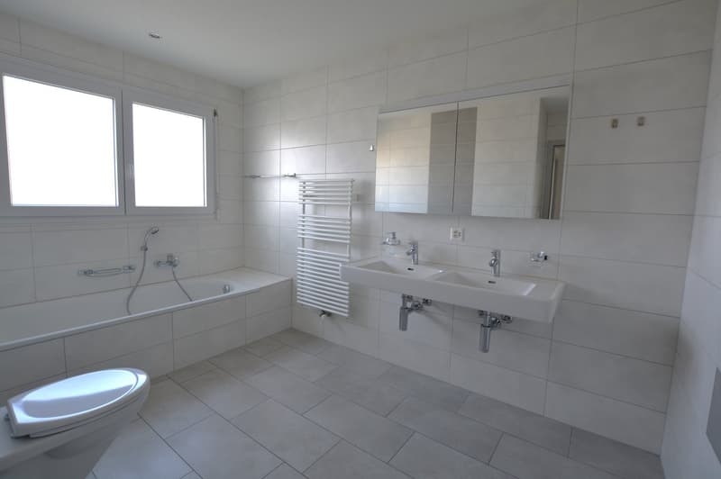 Fully white tiled bathroom, bathtub, sink, toilet, white tiled flooring