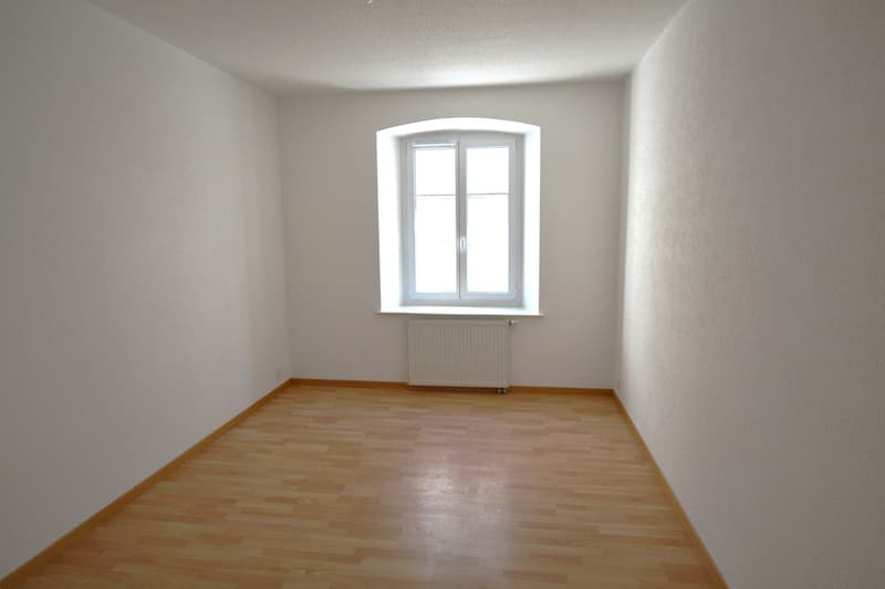 Empty room, wooden floor, white walls, arched window, radiator
