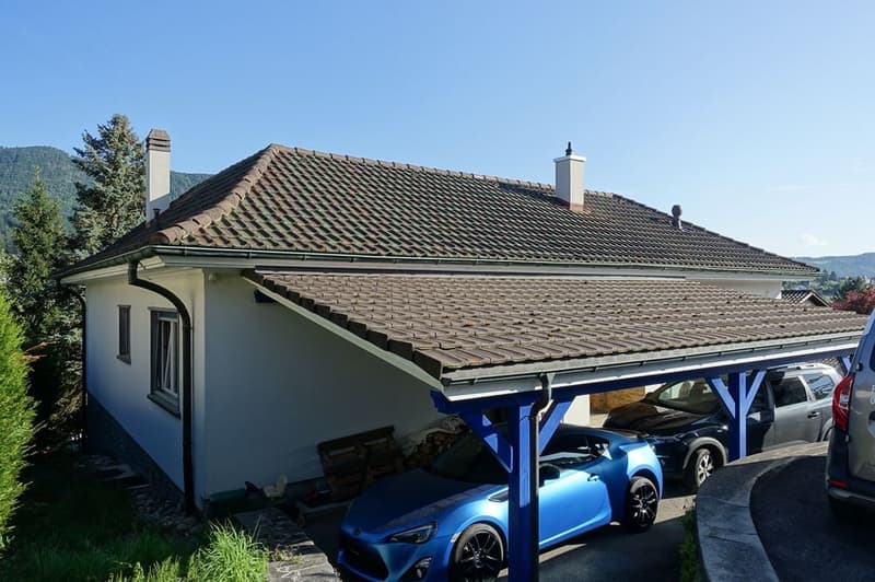 white house, brown roof, 2 chimneys, carport with 2 cars parked, wooden shed