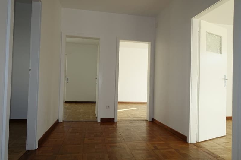 Open hallway with wooden floors, three open doors, clean white walls