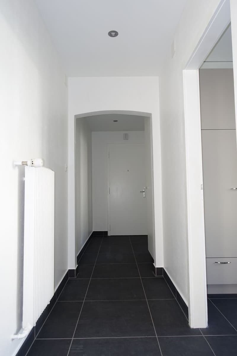 Corridor with white walls, tiled floor, a white radiator, and two doors