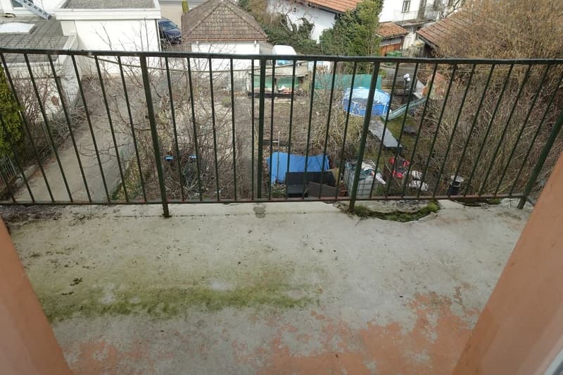 Balcony with metal railing, concrete floor, view of a backyard with various items
