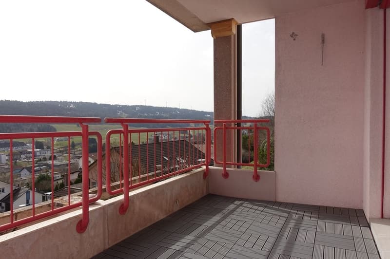 Balcony with red railings, wooden floor, view of the town