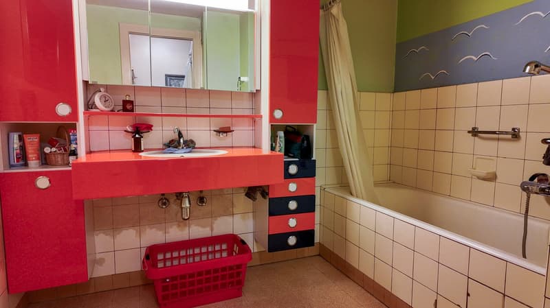 Bathroom with red cabinets, bathtub, sink, shelves with objects, tiled wall