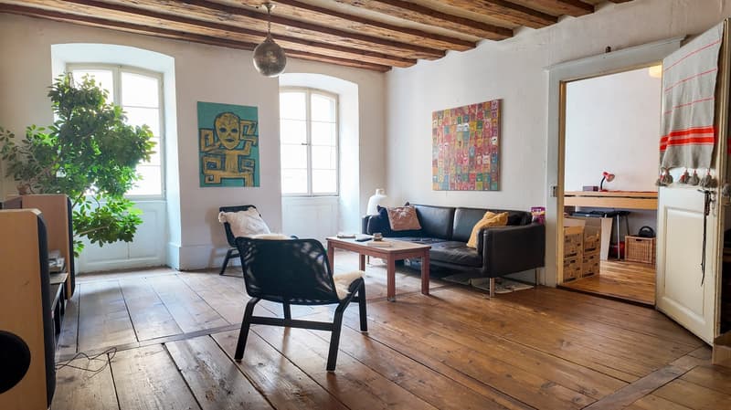 wooden floor, sofa, coffee table, armchair, plant, two paintings, wooden ceiling