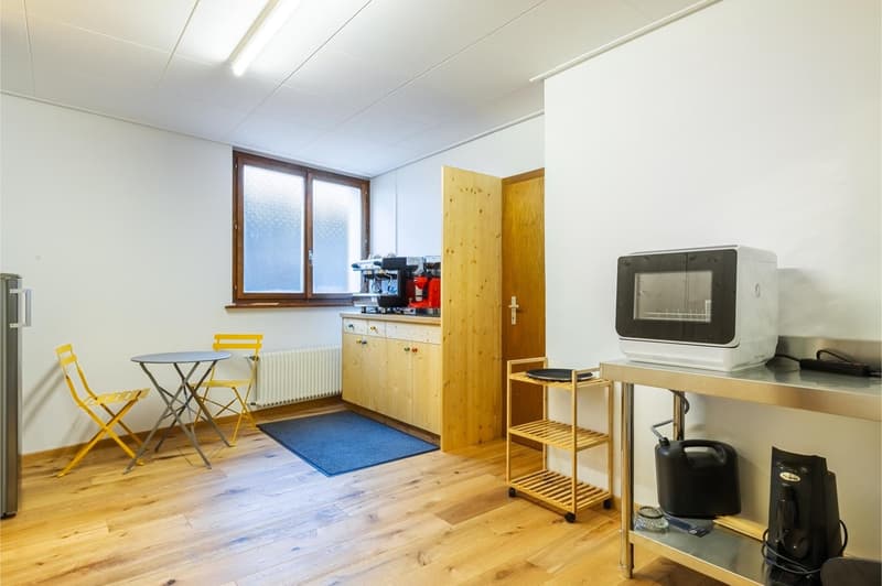Wooden floor, white walls, round table with two chairs, blue rug, kitchen appliances, refrigerator, microwave