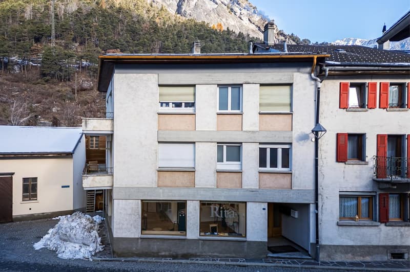 multistory building, white exterior, red shutters, sloping roof, mountain backdrop, ground floor store