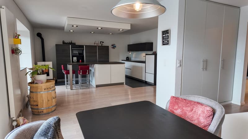 modern kitchen with dining area, wooden floor, white and black color scheme, kitchen island, modern appliances, potted plants, chandelier, red cushions on bar stools
