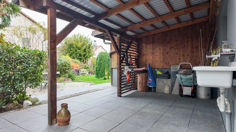 shed covered by wood with iron roof, open sides, washing station with white sink, trash bin, trolley, metal stand for tools