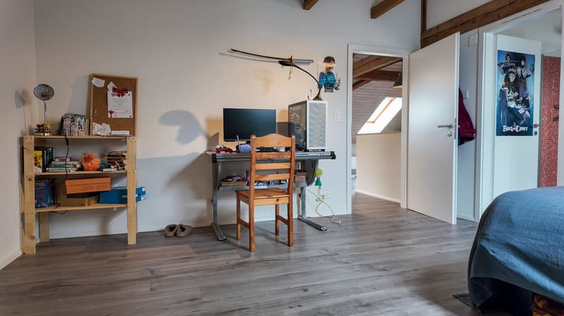 wooden desk with chair, computer monitor, shelves with books and toys, bed with blue blanket