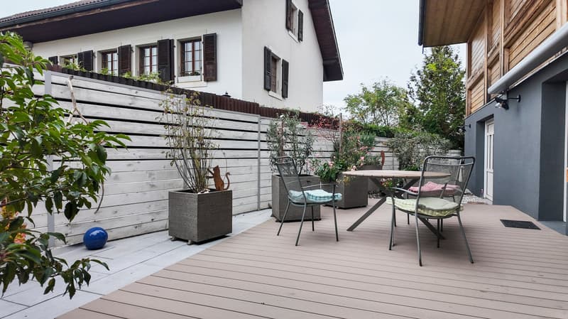 Table and chairs on deck with wooden railing, potted plants, and decorative items.