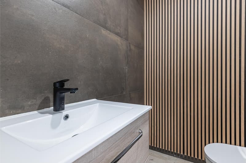 modern bathroom with white sink, black faucet, wooden wall paneling, white toilet