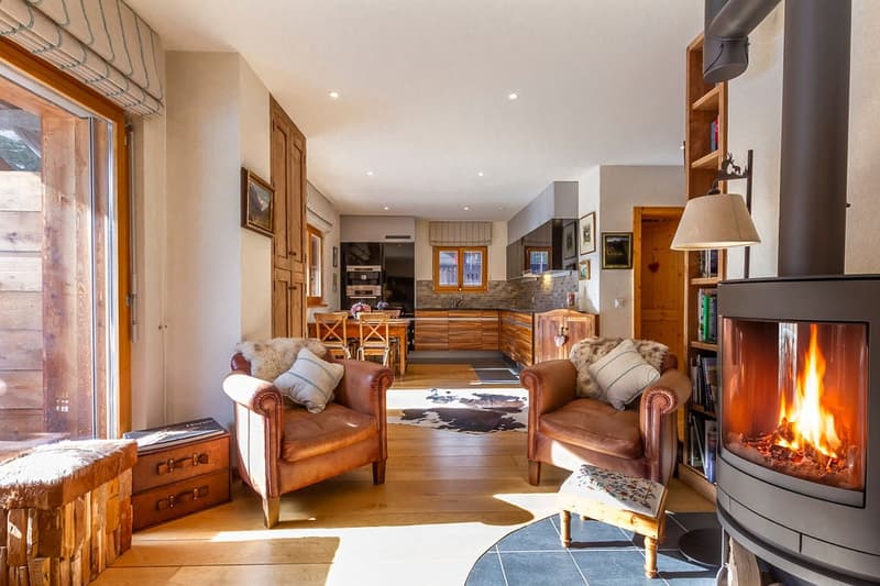 Cozy living room with a fireplace, leather armchairs, wooden furniture, and an open kitchen area