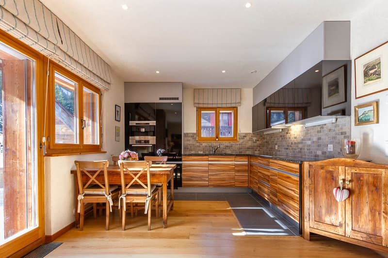 Spacious kitchen with wooden cabinets, stone backsplash, wooden dining table and chairs, and a dishwasher visible