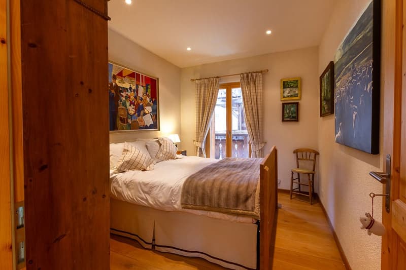 Spacious bedroom with wooden furniture, large bed, curtained windows, artwork on the walls, and a wooden chair in the corner