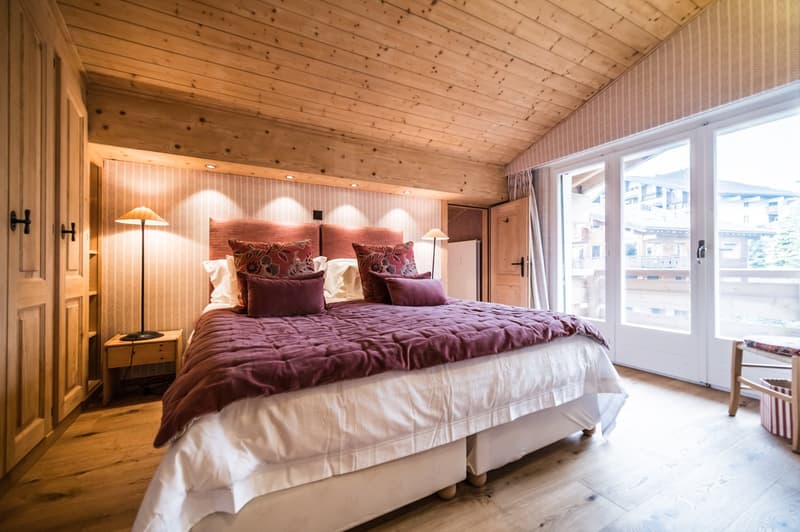 wooden ceiling and walls, double bed with pillows, nightstand with lamp, sliding glass door, wooden floor