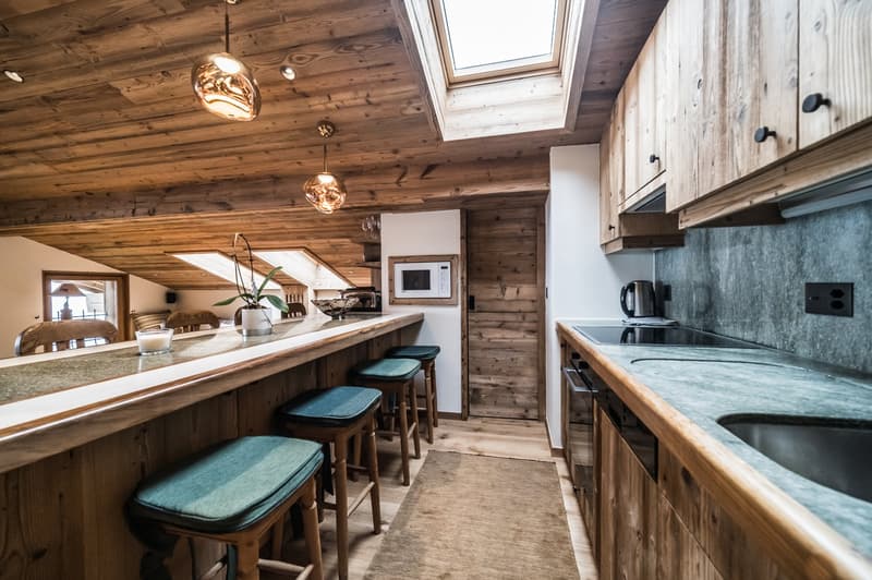 kitchen counter with bar stools, wooden cabinets, granite countertop, wooden flooring, microwave, electric kettle, stove top, refrigerator, sink