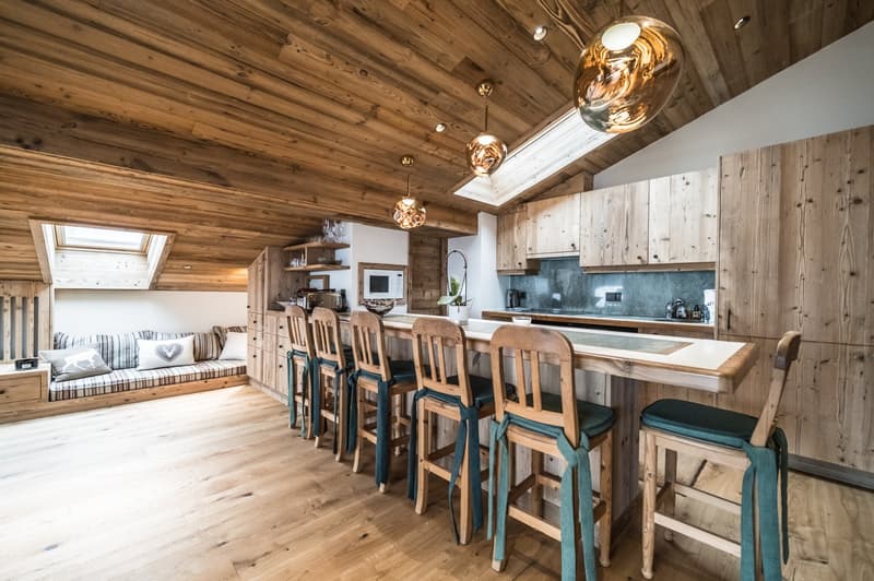 open kitchen with dining bar, wooden countertops, island, wooden ceiling, kitchen cabinets, natural wooden flooring, skylights, kitchen island with bar stools, seating area with couch and pillows, counter with microwave