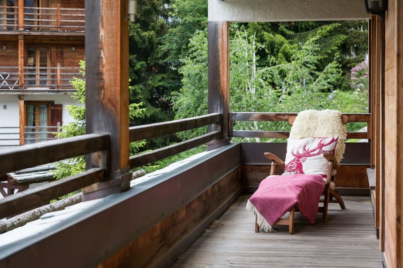 Balcony with wooden railing, wooden chaise lounge, blanket, pillow, view of green landscape