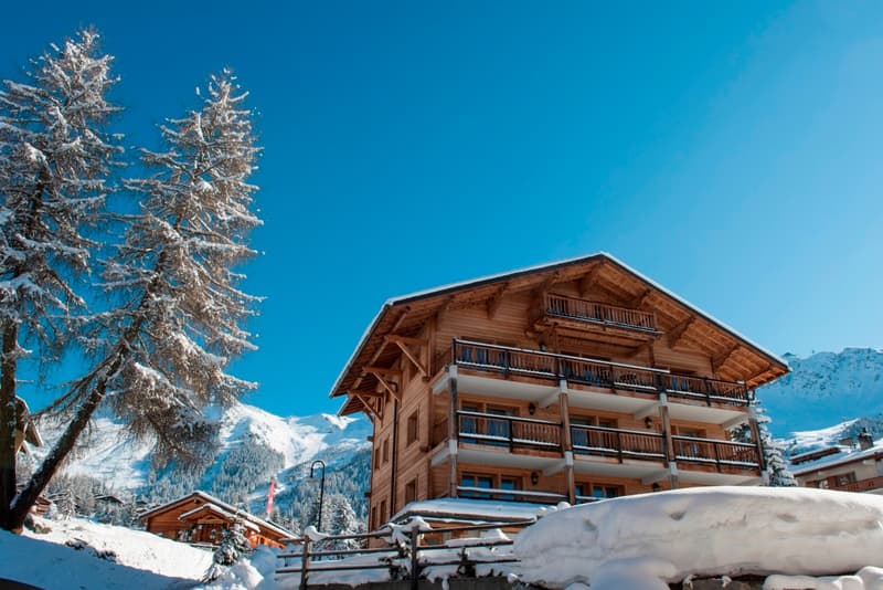 modern wooden house, multiple balconies, covered snow, snowy mountains in the background