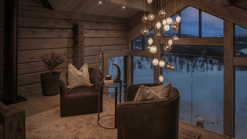 wooden cabin interior, carpet, cozy seating with pillows, round table, chandelier, large windows