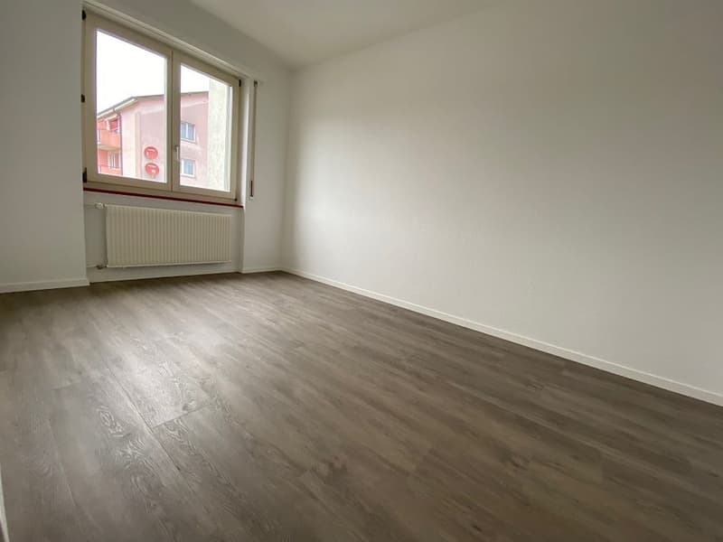 Spacious bedroom with large windows, white walls, and laminate flooring in a neutral gray tone