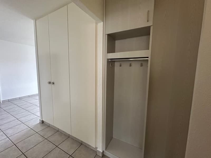 The image shows a bedroom with a built-in wardrobe, tile flooring, and neutral-colored walls.