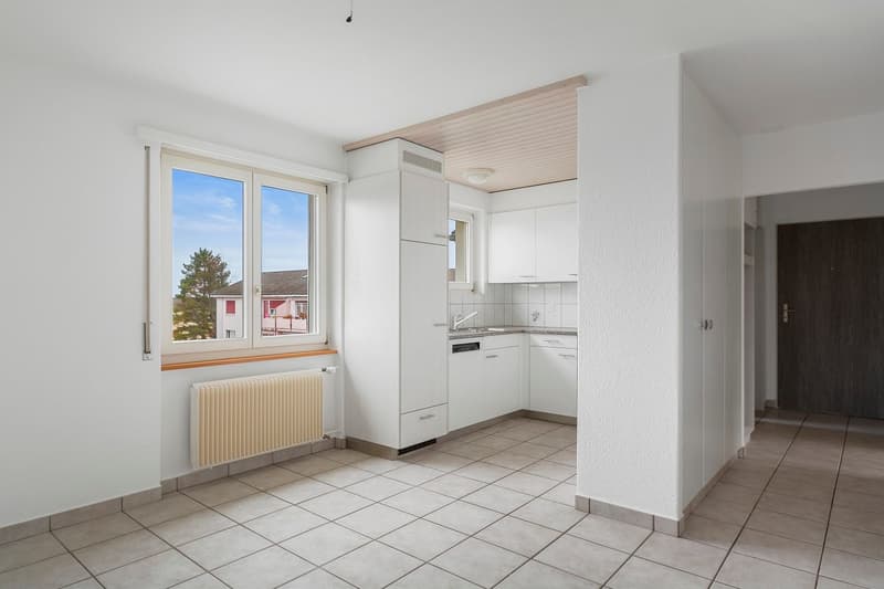 Spacious kitchen with white cabinets, tiled floor, and large windows providing natural light. The kitchen appears to be equipped with a dishwasher.