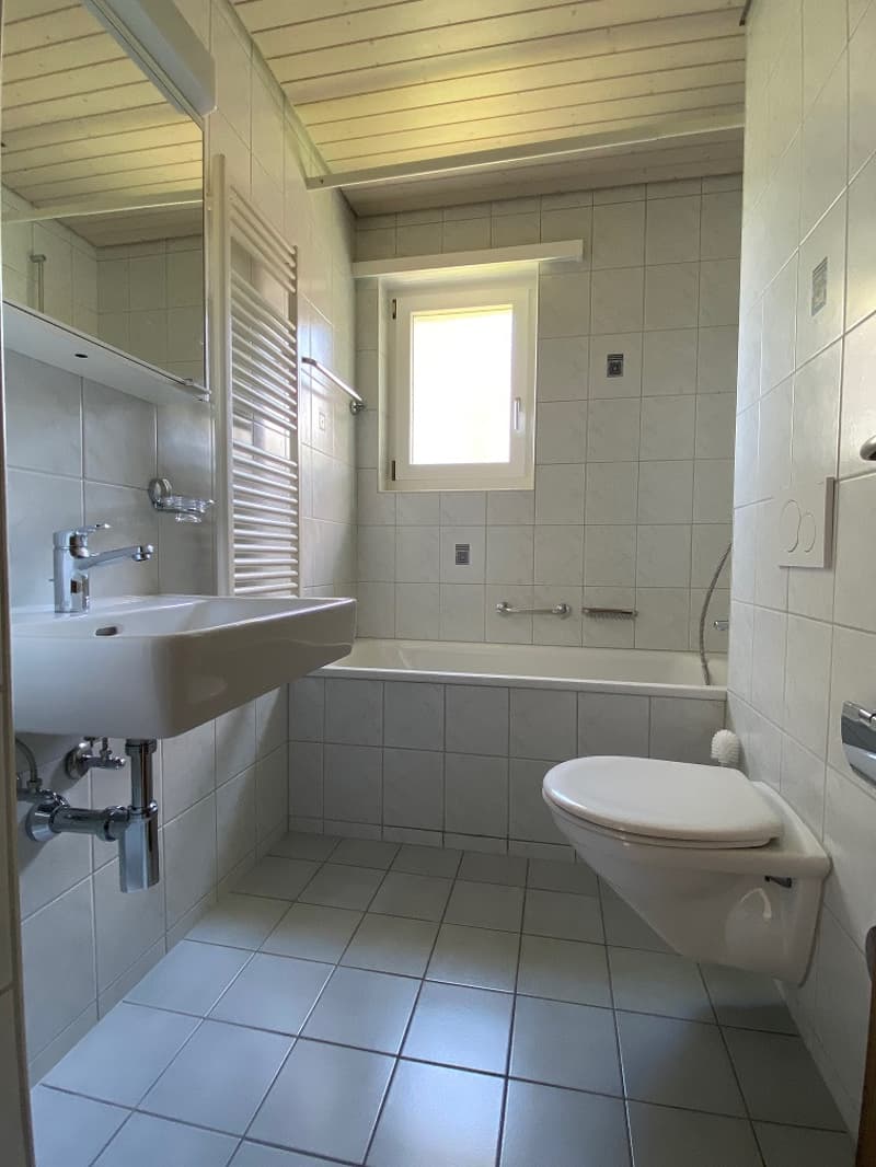 white tiled walls, white tiled floor, sink with mirror, toilet, shower area, window