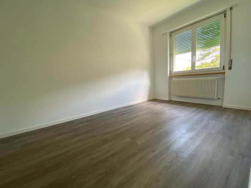 empty room, white walls, wooden floor, single window with blinds, white radiator