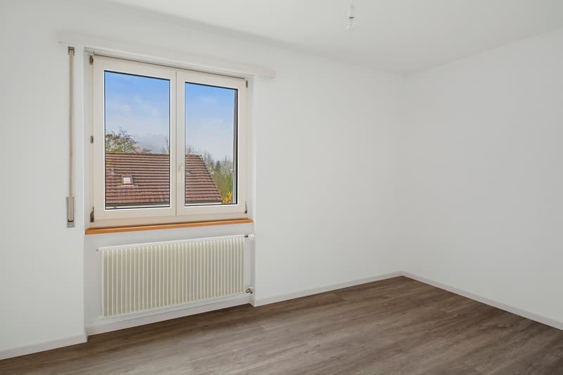 empty room with white walls, wooden floor, radiator, window with outdoor view