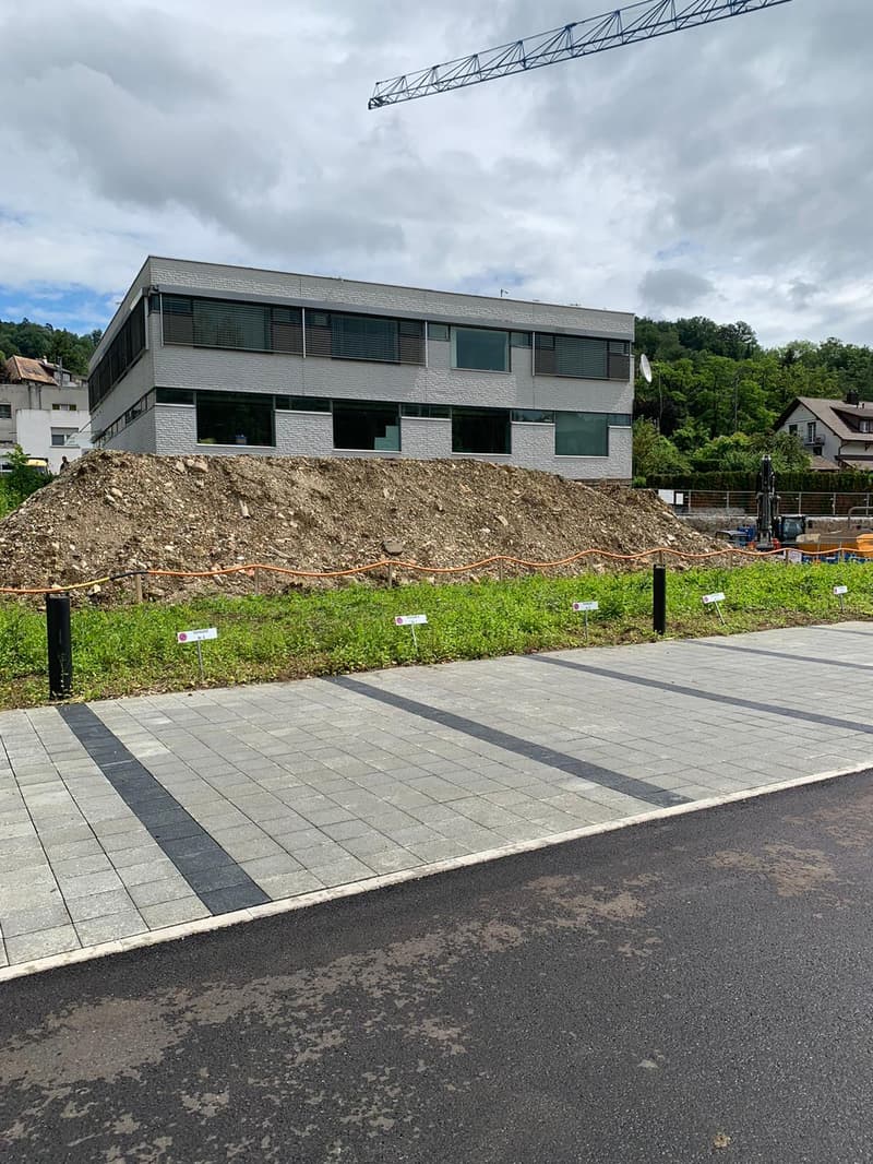Building under construction, ground floor, large dirt pile in front, sidewalk, trees