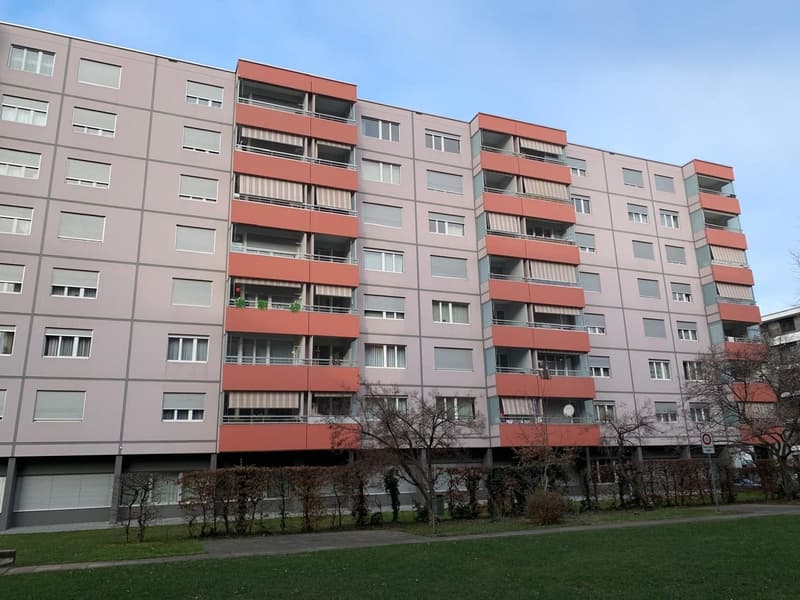 4 story apartment building, gray walls, red balconies, multiple windows, greenery around