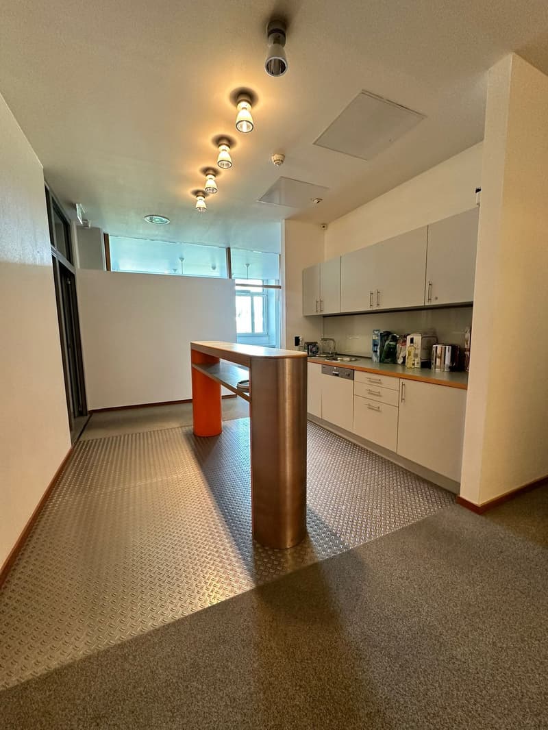Spacious kitchen with white cabinets, wooden countertop, and a dishwasher. The room has a modern lighting system with multiple spotlights on the ceiling. The floor is covered with a textured tile pattern.