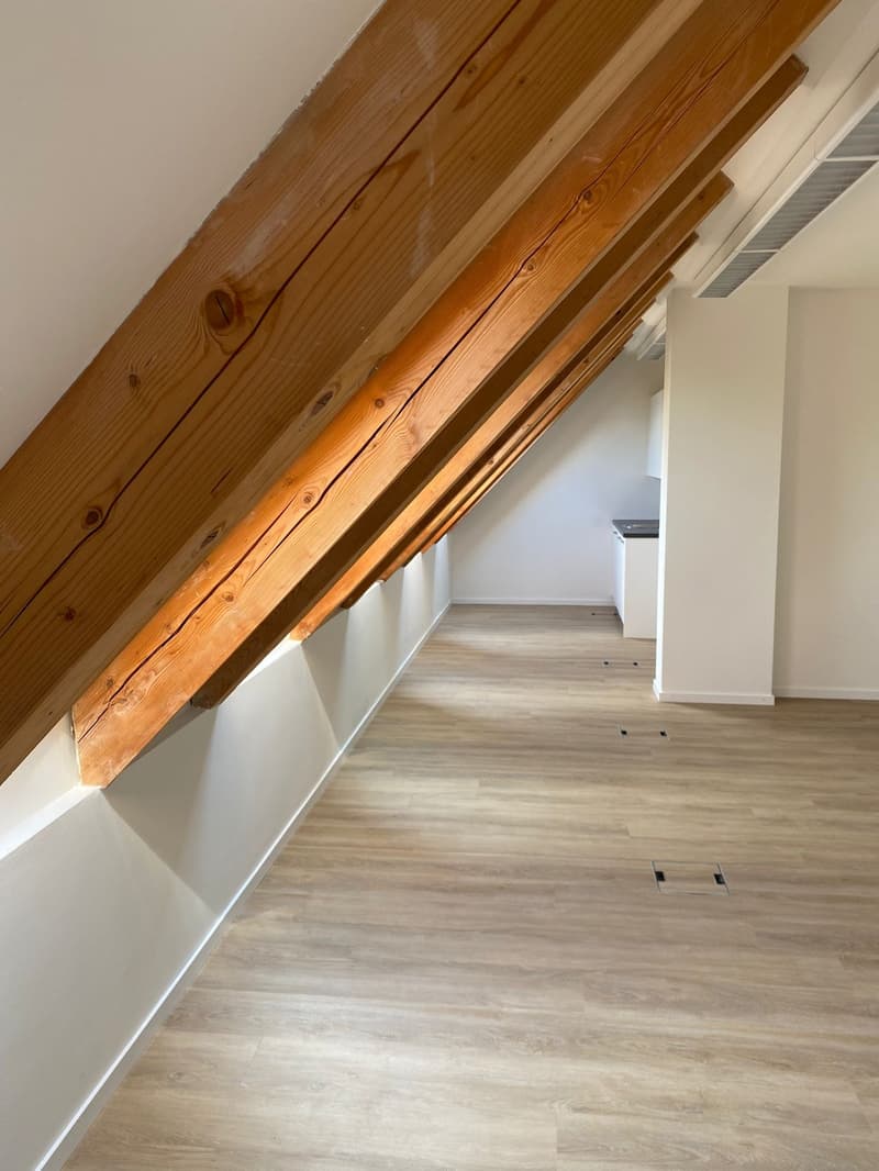 empty attic room, wooden beams, hardwood floors, windows on the side, small kitchen area