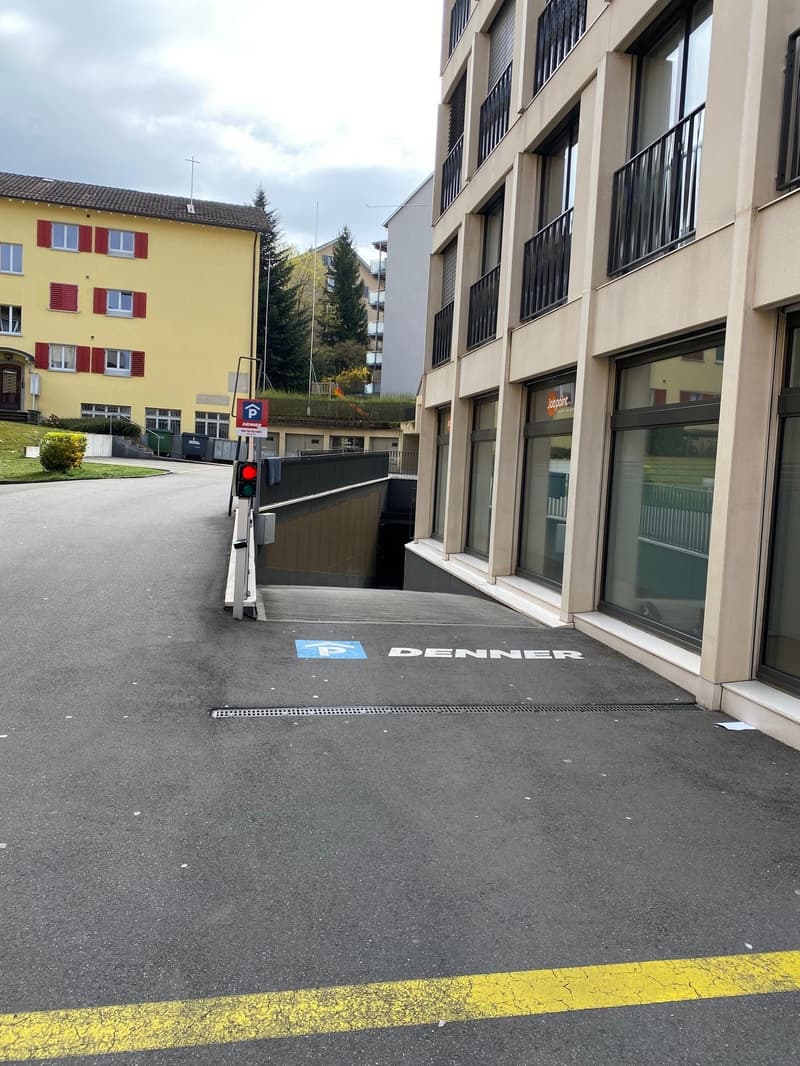 Parking area with a building entrance, a yellow line, and a sign indicating parking.