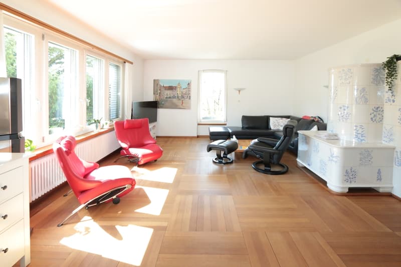 Wohnbereich mit schönem Kachelofen / a living room with wood floors, a red chair and a television